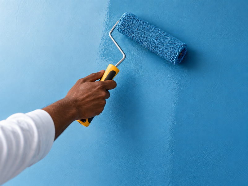 Artisan ivoirien appliquant une peinture bleue au rouleau sur un mur