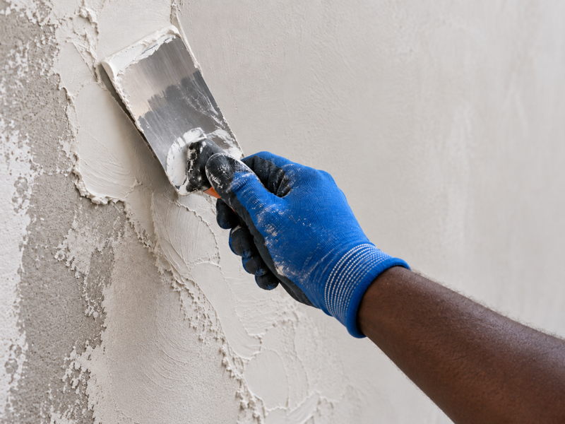 Artisan ivoirien appliquant un enduit de préparation sur un mur avant peinture